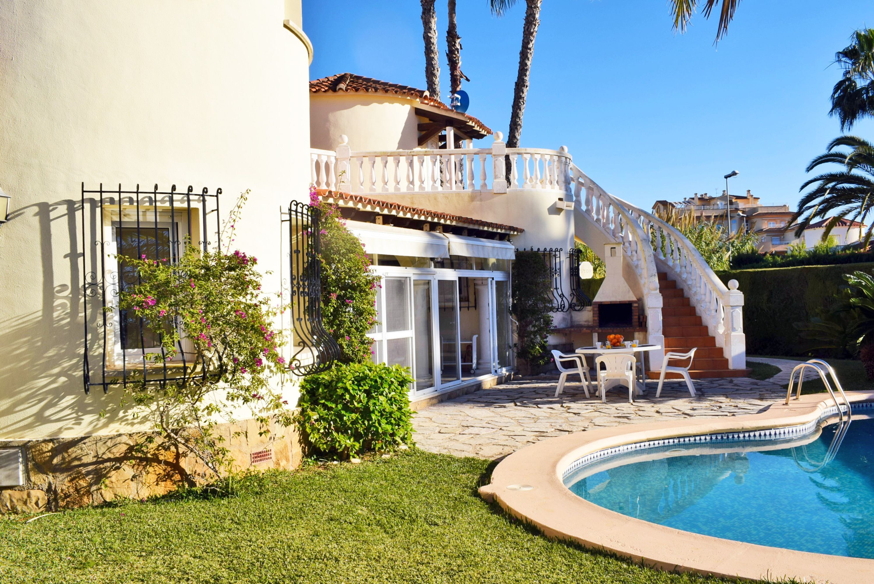 A poolside area with a curved pool, outdoor furniture, and a staircase leading to a balcony.