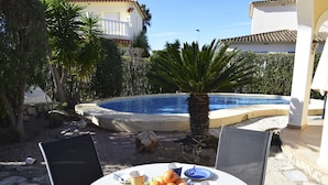 A poolside table with fruits and cups, surrounded by chairs, with a pool and palm trees in the background. - Ch1400 in Oliva With 2 Bedrooms and 2 Bathrooms (Oliva)