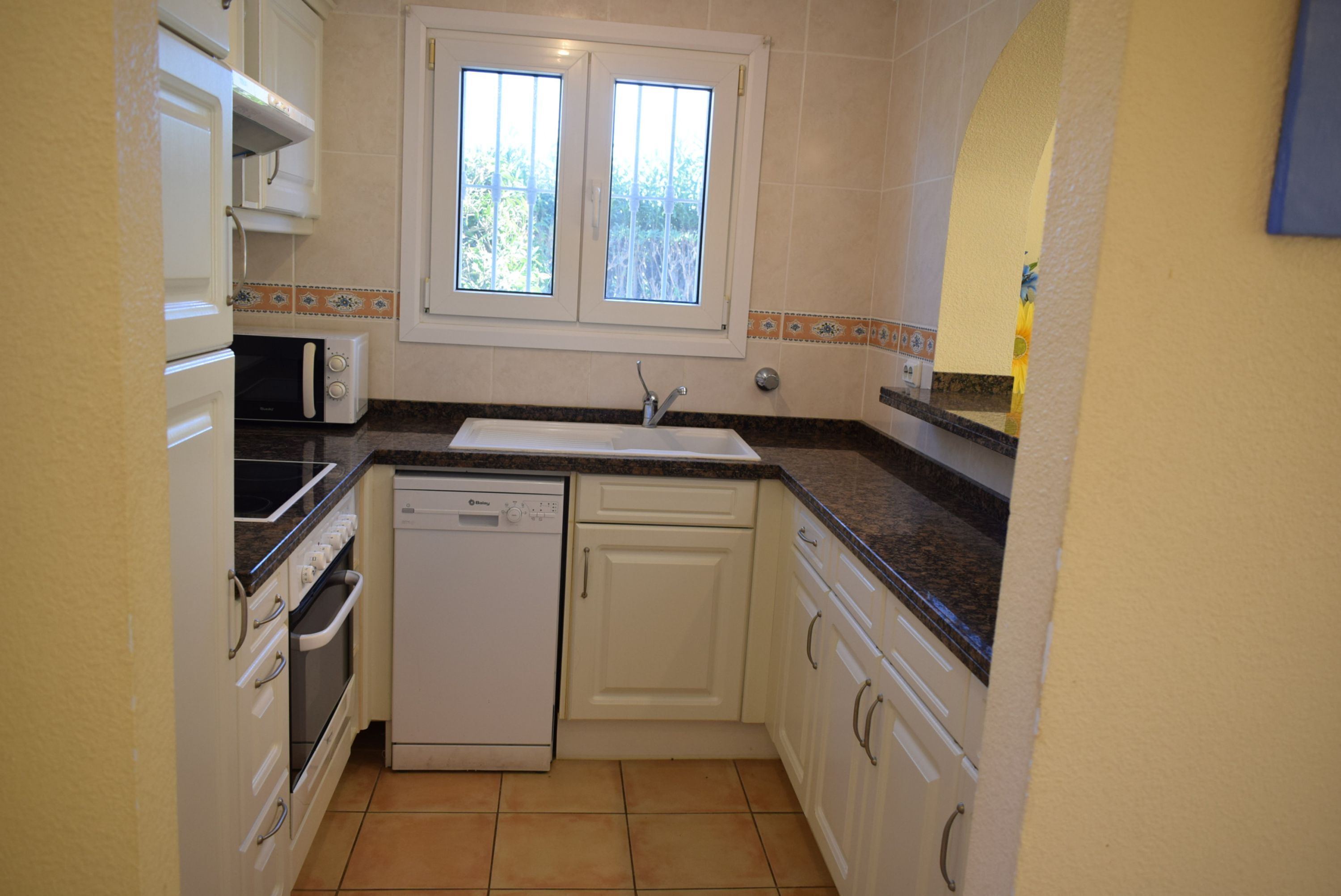 A compact kitchen with a dishwasher, oven, microwave, and a window above the sink.