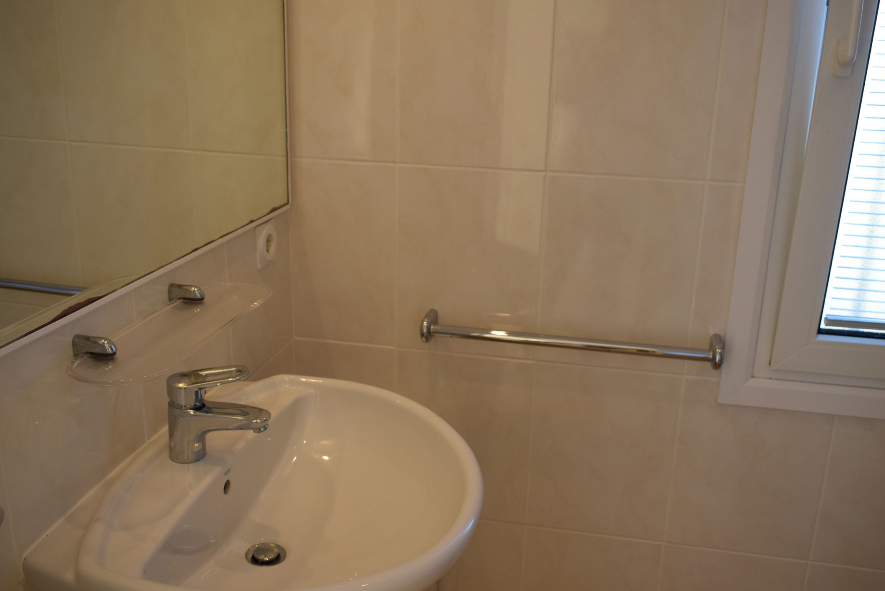 A bathroom with a sink, mirror, and handrail.