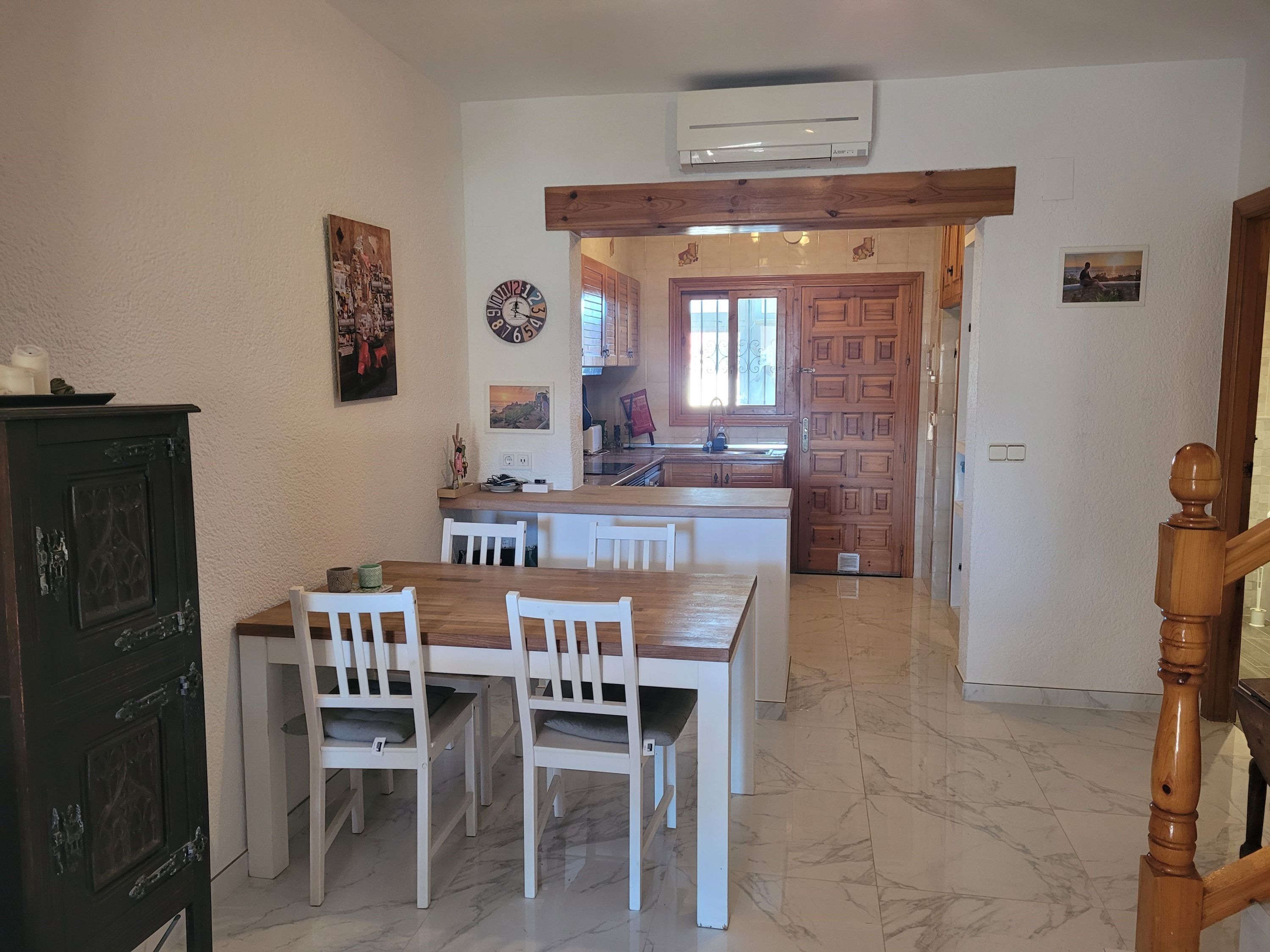 A kitchen with a wooden table and chairs, a clock, and a door leading to another room.