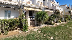 A white building with a yellow awning, a small patio, and a garden with various plants. - Dup2136 in Denia With 2 Bedrooms and 1 Bathrooms (Denia)