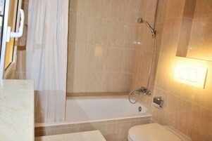 Baño con bañera, ducha, inodoro y espejo.