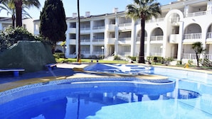 A swimming pool with a tiled edge, surrounded by a building with multiple balconies and a palm tree. - Ap611 in Oliva With 2 Bedrooms and 1 Bathrooms (Oliva)