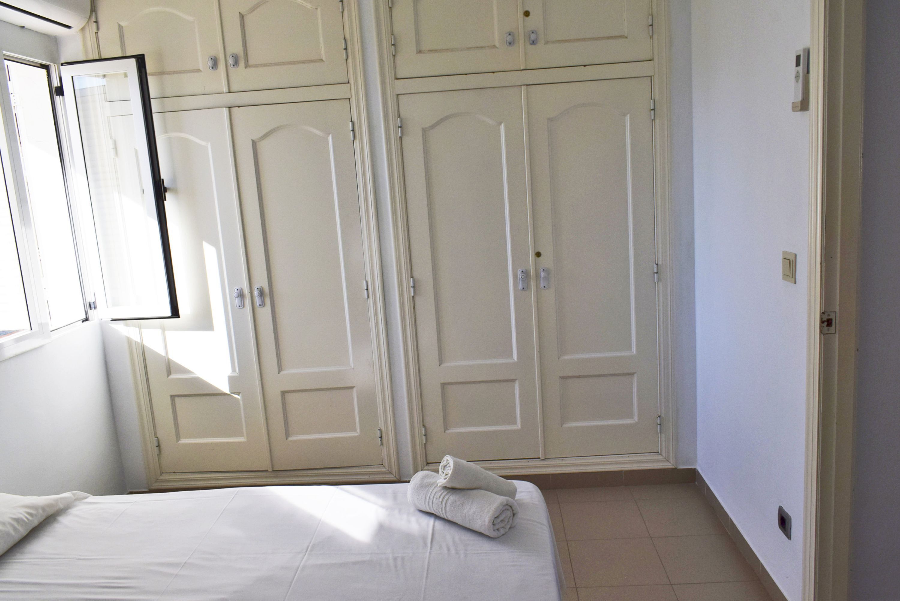 A hotel room with a bed, a window, and a set of double doors.