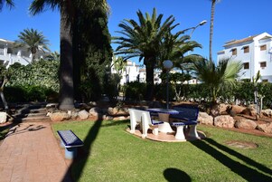 Un patio con mesa y sillas, rodeado de palmeras y un muro de piedra.