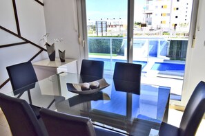 A modern dining area with a glass table and black chairs, overlooking a pool and buildings. - Ap2700 in Oliva With 2 Bedrooms and 2 Bathrooms (Oliva)