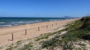Een zandstrand met een houten omheining en begroeiing.