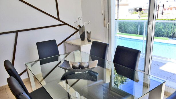 Een moderne eetruimte met een glazen tafel, zwarte stoelen en uitzicht op een zwembad.