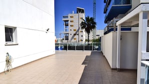 Een modern gebouw met een betegeld terras, een palmboom en een bouwkraan op de achtergrond.