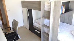 Een stapelbed met bureau en stoel, een boekenplank en een deur.