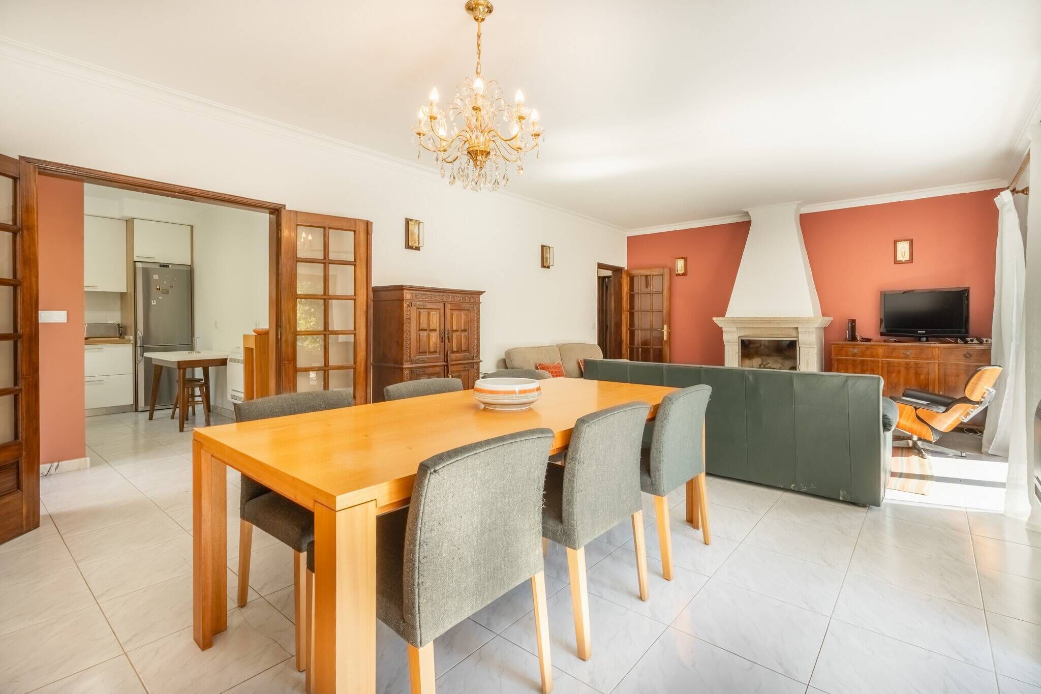 Uma sala de estar espaçosa com uma mesa de jantar de madeira, cadeiras estofadas cinzas, lareira e televisão.