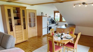 Una sala de estar acogedora con un mueble de madera, una mesa de comedor para dos personas y una cocina al fondo.