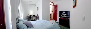 A hotel room with a bed, a desk with a chair, a TV, and a door leading to a bathroom. - Casa Ángel (Morelia)