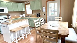 Una cocina con armarios verdes, una mesa de comedor de madera y sillas blancas.