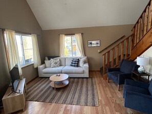 A living room with a sofa, a coffee table, a TV on a stand, and a staircase.