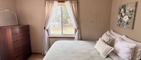 Een slaapkamer met een houten dressoir, een bed met een gestreept laken en een plafondventilator, en een raam met gordijnen.
