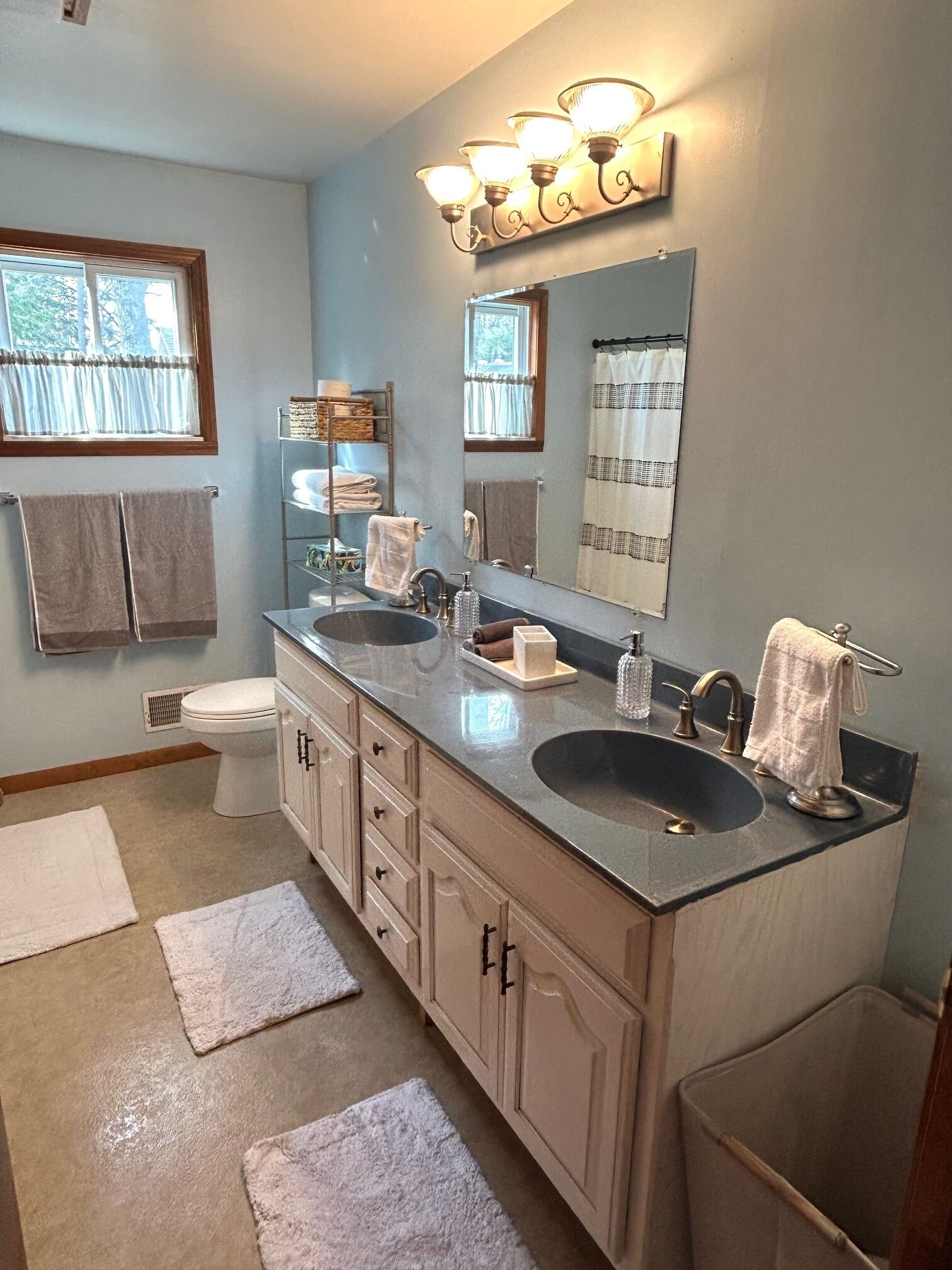 Une salle de bain avec deux lavabos, des toilettes, un miroir et une fenêtre avec des rideaux.