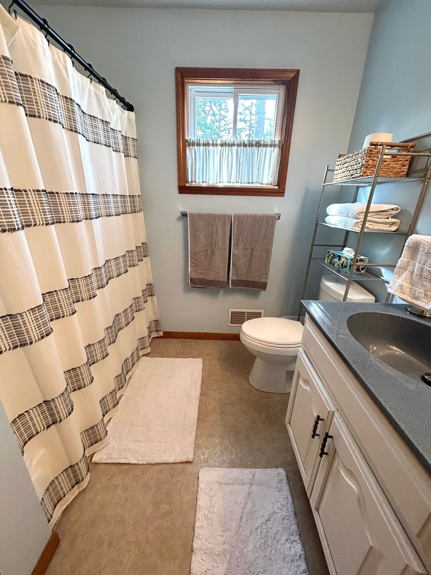 Une salle de bain avec un rideau de douche, une fenêtre, des toilettes, un lavabo et un porte-serviettes.