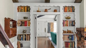 Une bibliothèque avec des étagères de part et d’autre d’une porte centrale, qui donne sur une pièce où se trouve un canapé vert.