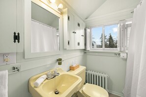 Ein Badezimmer mit einem gelben Waschbecken, einer weißen Toilette und einem Fenster mit Blick auf Bäume.