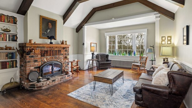 Un salon chaleureux avec une cheminée en briques, un plancher en bois, des meubles en cuir et de grandes fenêtres.
