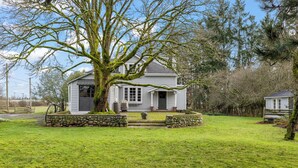 Une maison blanche avec des fondations en pierre, un grand arbre devant et un mur de pierre qui entoure la propriété.