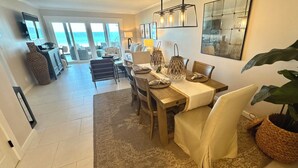 A spacious living area with a dining table, chairs, and a large plant. There is a kitchen area with a counter and a television mounted on the wall. - Ocean 382 -First Floor Beachfront Condo2 bedrooms/2 baths (Ponte Vedra Beach)