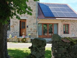 A stone building with a solar panel roof, a wooden door, and a stone wall. - La Picolina - CHARENSAT (CHARENSAT)