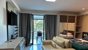 A hotel room with a sofa, a bed, a TV, and a balcony with a table and chairs. - Flat Premium Vista Mar - Praia de Tabatinga (Conde)