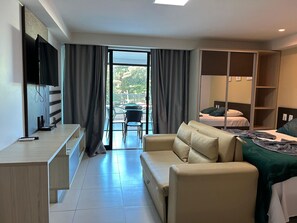 A hotel room with a sofa, a bed, a TV, and a balcony with a table and chairs. - Flat Premium Vista Mar - Praia de Tabatinga (Conde)