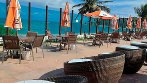 A beachside lounge area with wicker furniture and orange umbrellas, overlooking the ocean. - Flat Premium Vista Mar - Praia de Tabatinga (Conde)