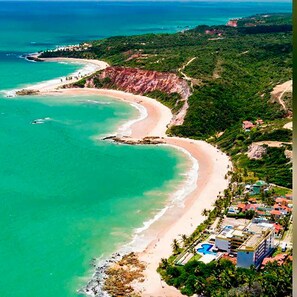 An aerial view of a coastal area with a beach, cliffs, and a resort with multiple buildings. - Flat Premium Vista Mar - Praia de Tabatinga (Conde)