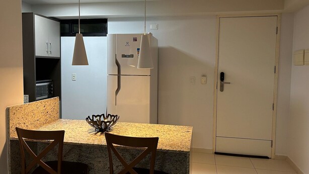 A compact kitchen with a dining area, featuring a refrigerator, microwave, and a small cabinet. - Flat Premium Vista Mar - Praia de Tabatinga (Conde)