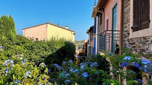 Un edificio de piedra tradicional con un jardín delantero, con flores azules y un cielo azul despejado.