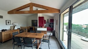 Una cocina moderna con gabinetes rojos, un comedor con mesa y sillas de madera, y un ventanal que ofrece vistas de la ciudad.