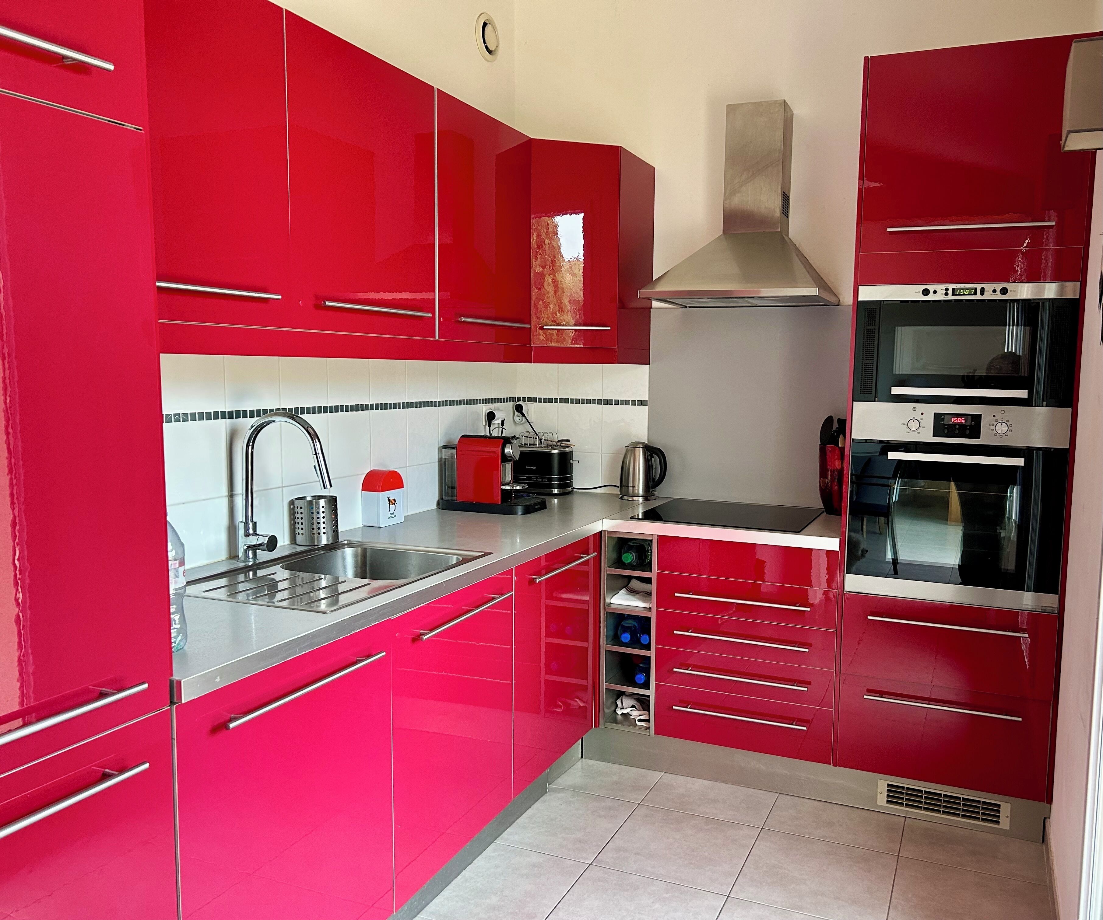 A kitchen with red cabinets, stainless steel appliances, and a tiled backsplash.