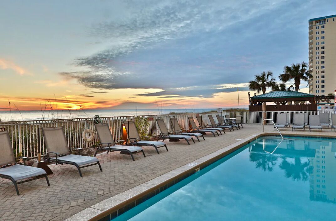 Un espace aménagé au bord de la piscine, avec des chaises longues et une vue sur le coucher de soleil sur l’océan.