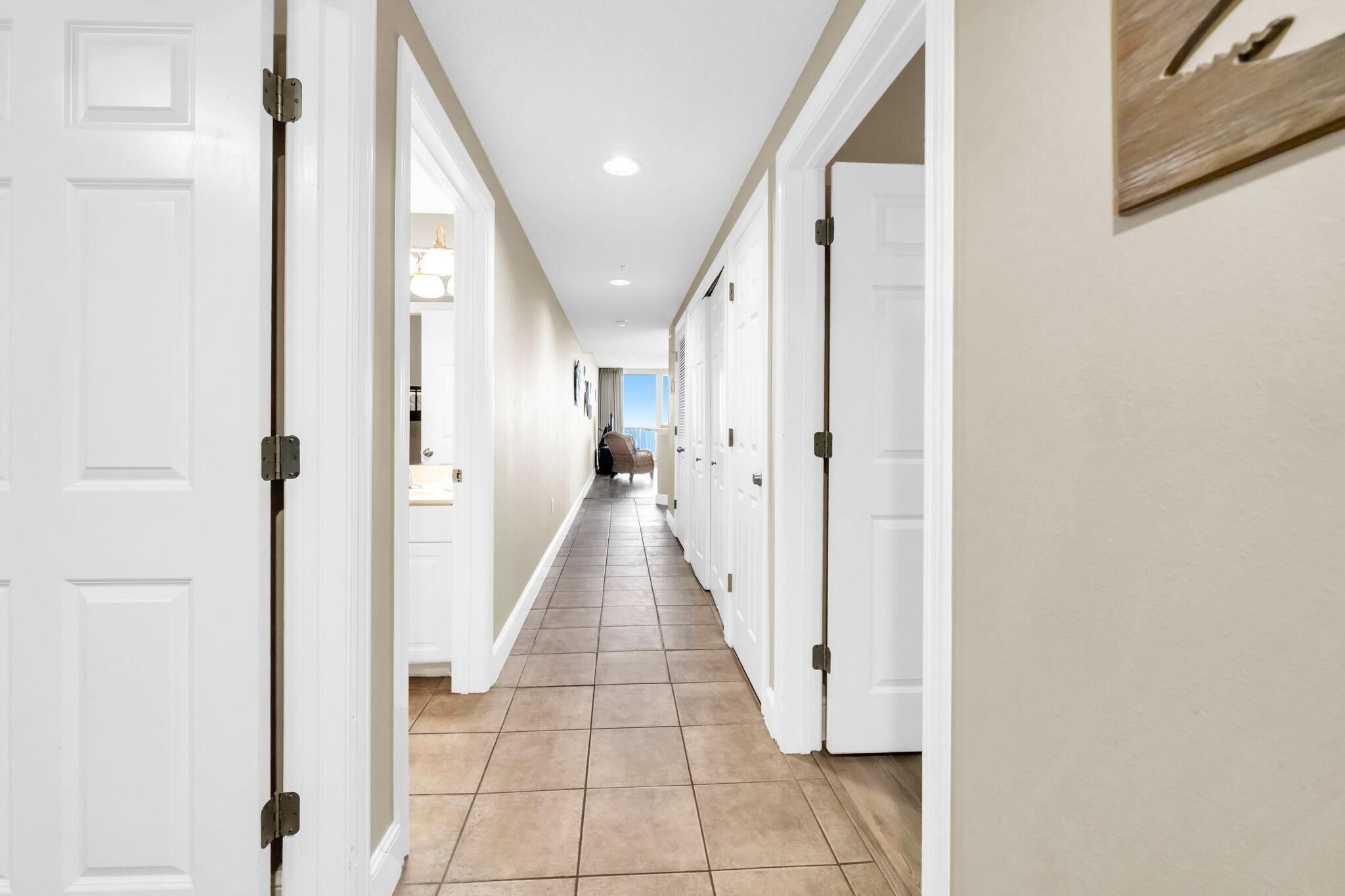 A hallway with white doors, beige walls, and a tiled floor.