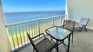 Uma varanda com mesa de vidro e duas cadeiras, com vista para a praia e o oceano.