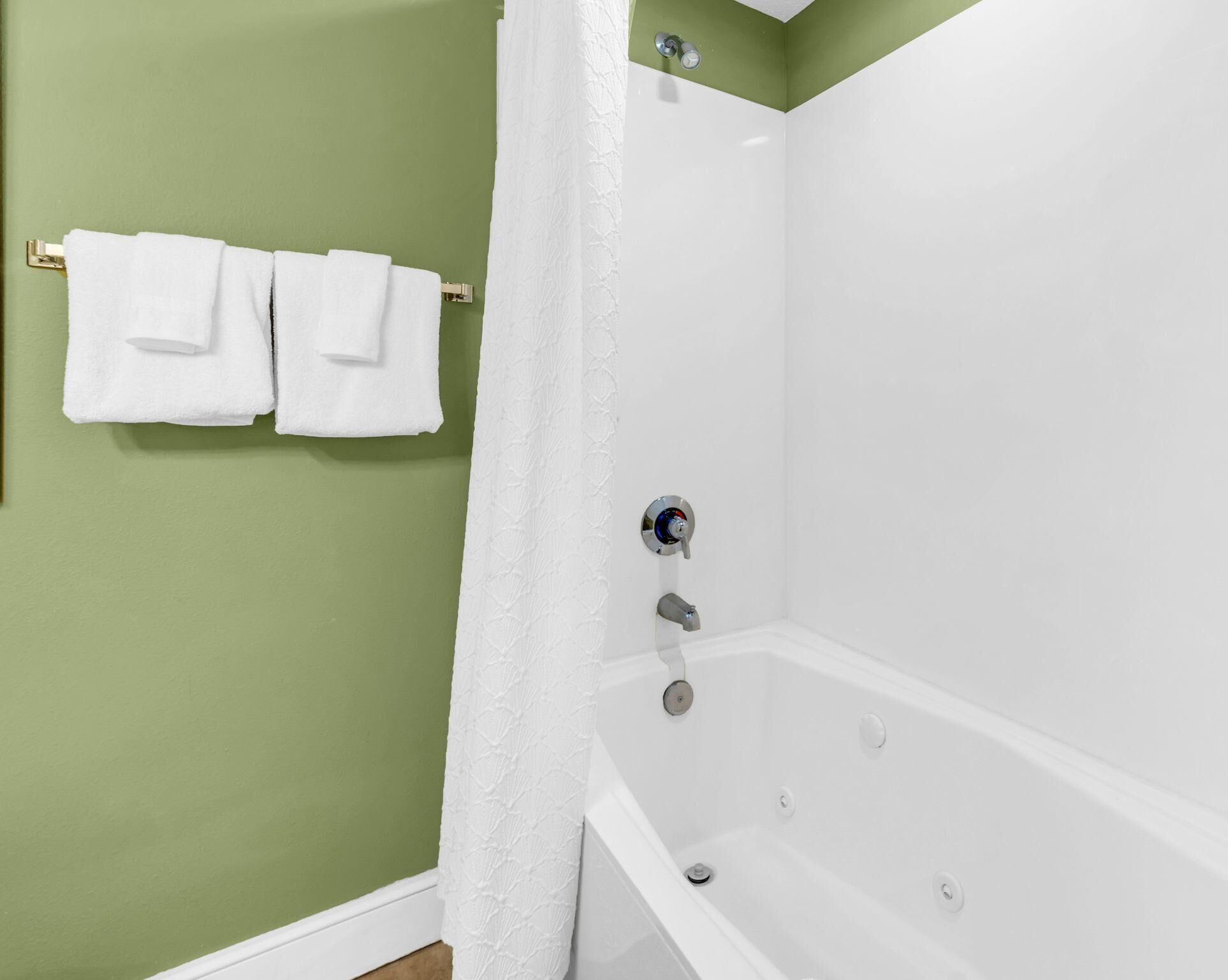A bathroom with a white bathtub, green walls, and two white towels hanging on a towel rack.