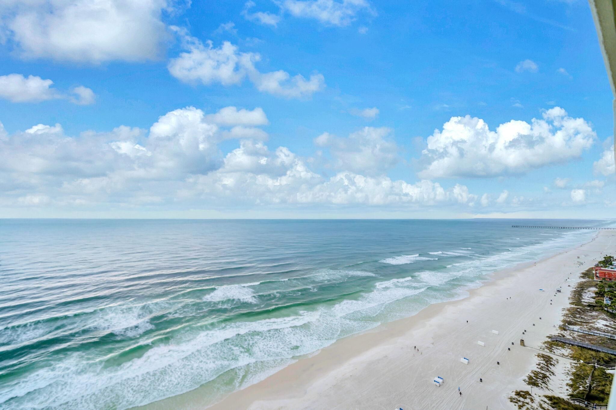 A beach with a pier extending into the ocean, clear skies, and a few people on the sand.