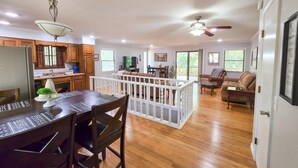A spacious living area with a wooden floor, a dining table with chairs, a white railing, and a ceiling fan. - 4BR/2BA with Huge Deck, Bonus Room, Swimming/Fishing & Stunning Seasonal Views! (Mountain Home)