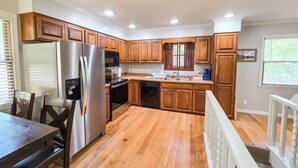 A modern kitchen with wooden cabinets, stainless steel appliances, and a wooden dining table. - 4BR/2BA with Huge Deck, Bonus Room, Swimming/Fishing & Stunning Seasonal Views! (Mountain Home)