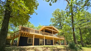A two-story wooden cabin with a balcony, surrounded by trees. - 4BR/2BA with Huge Deck, Bonus Room, Swimming/Fishing & Stunning Seasonal Views! (Mountain Home)