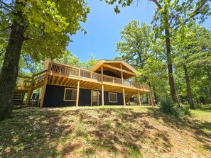 A two-story wooden cabin with a balcony, surrounded by trees. - 4BR/2BA with Huge Deck, Bonus Room, Swimming/Fishing & Stunning Seasonal Views! (Mountain Home)