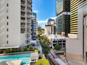 A modern urban hotel with multiple floors, a swimming pool, and a mix of residential and commercial buildings in the background. - River View 1BR w/ Balcony and Pool Access (Brisbane)