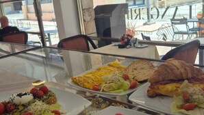 A restaurant with outdoor seating, various dishes on plates, and a view of the street through large windows. - All Inclusive MDH (Cancun)