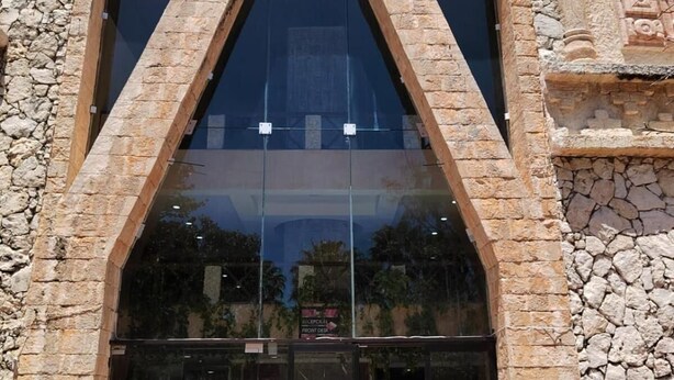 A building with a stone facade, large glass entrance, and potted plants in front. - All Inclusive MDH (Cancun)