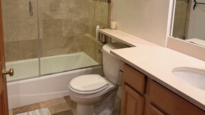 Un bagno con cabina doccia in vetro, un water bianco, una vasca da bagno e mobili in legno.